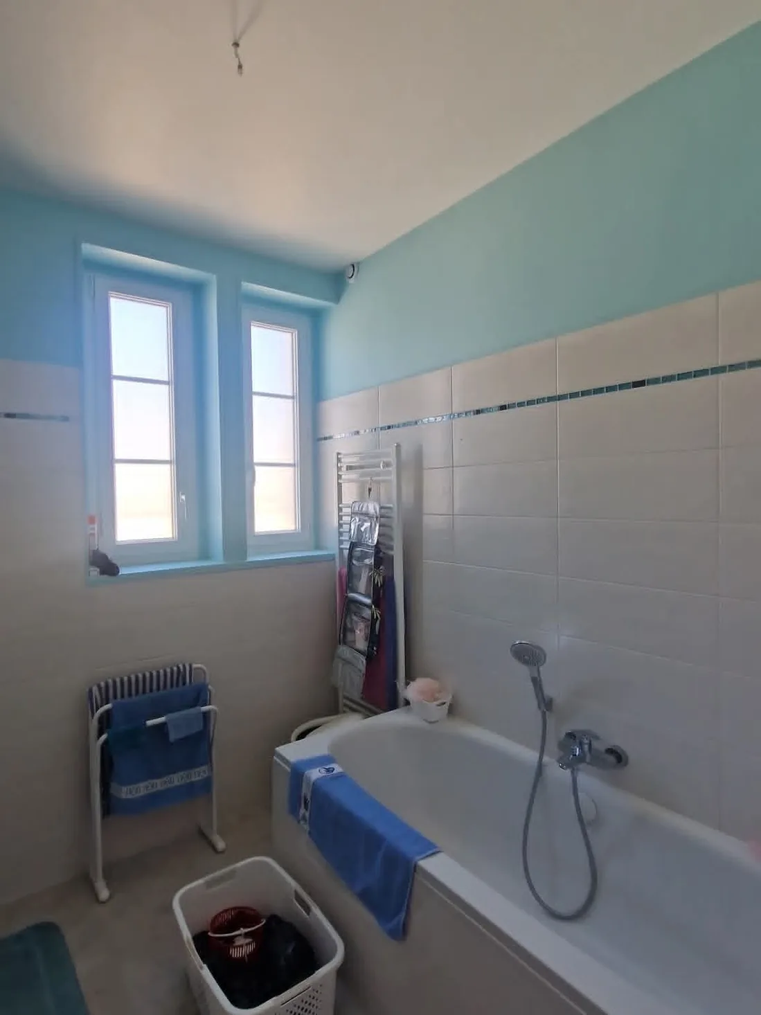 Salle de bain — côté fenêtre après travaux : Faïence blanche, murs en vert d’eau et plafond repris.